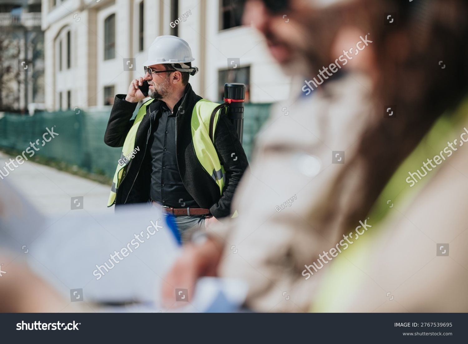 stock photo construction site manager wearing a hard hat and high visibility vest speaks on a mobile phone 2767539695